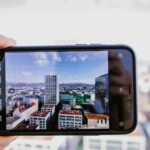 Smartfon w dłoni fotografujący miejską panoramę pod błękitnym niebem