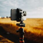 Smartfon na statywie fotografuje złote pole pod jasnym niebem