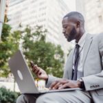 Biznesmen w garniturze korzysta z laptopa i smartfona w centrum miasta