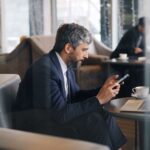 Biznesmen w garniturze korzysta ze smartfona i laptopa w kawiarni
