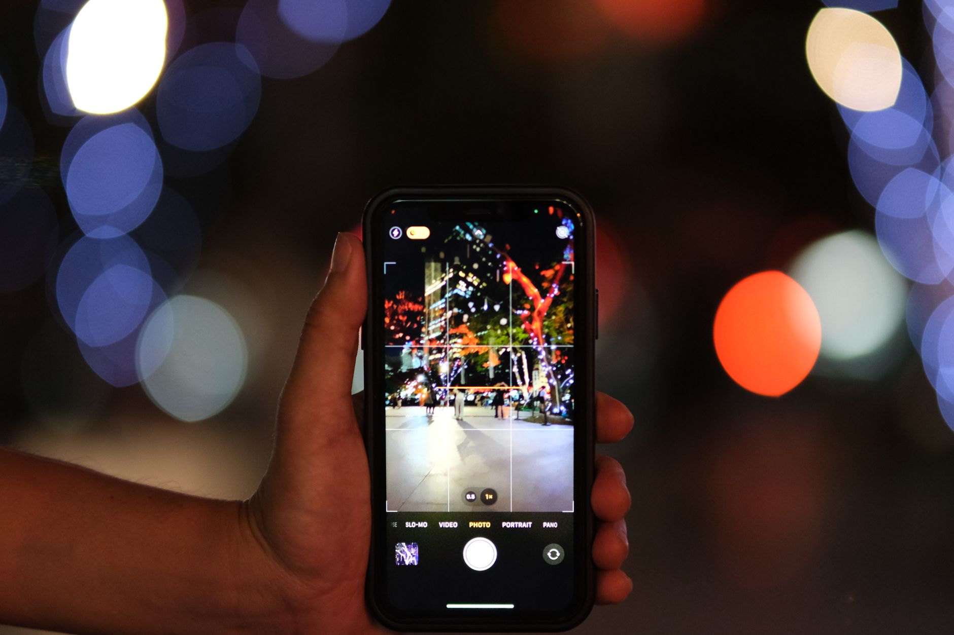 Zbliżenie na smartfon fotografujący nocne miasto z kolorowym bokeh