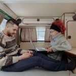 Para pracująca na laptopie i smartfonie w kampervanie podczas podróży