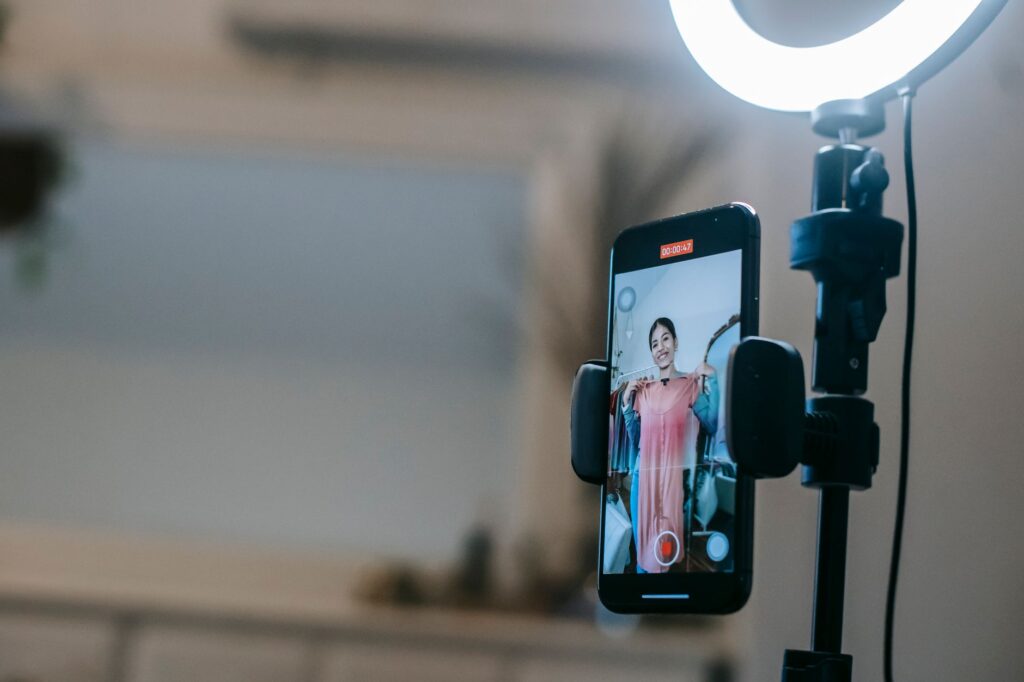 Blogerka nagrywa vlog smartfonem z lampą pierścieniową i różową sukienką
