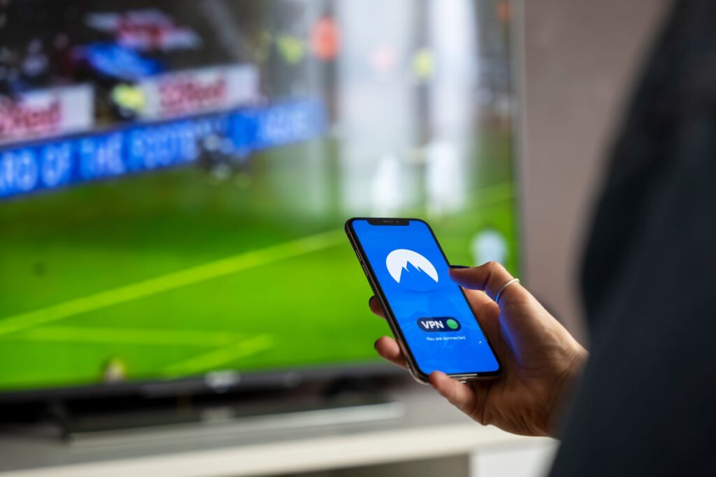 Osoba trzyma smartfon z aplikacją VPN podczas transmisji sportu na telewizorze